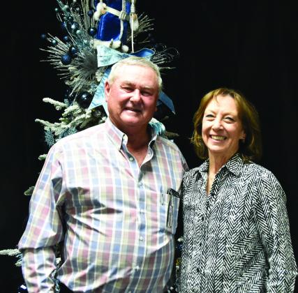 A BOW IN HIS HAIR—Through a photographic happenstance, Mike Brumley appears to have a blue bow in his hair, although it’s actually on the gorgeous tree behind him at the Festival of Trees Gala. All the same, his wife Janice flashes her characteristic million dollar smile. (Photo by Jim Steiert)
