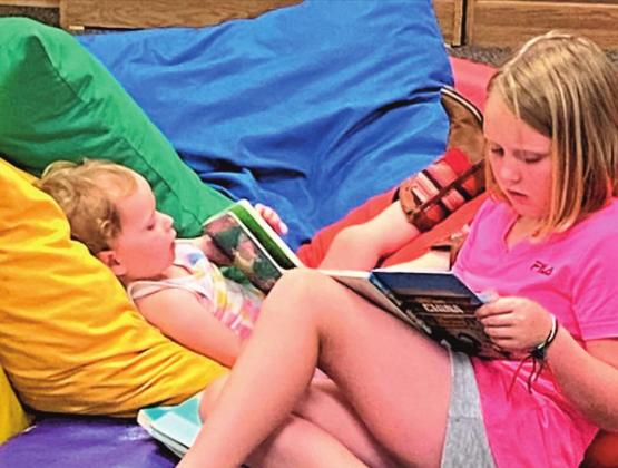 Mackenzie and Ivy Brown reading books at Rhoads Memorial Library during the Summer Reading Program.